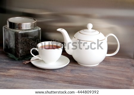 Tea pot, glass jar with fermented tea leaves, tea cup with brewing black tea. Wooden table, black background. Chinese porcelain.