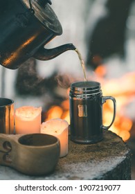 Tea is poured from kettle into campfire mug standing on a tree stump in winter forest
