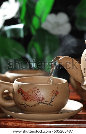 tea poured from a teapot into a clay cup on a blurred floral background