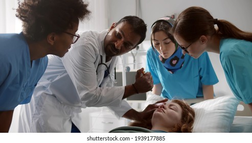 Tea of residential doctors examining patient in emergency room at hospital. Mature indian practitioner teaching young interns treating unconscious patient in hospital
