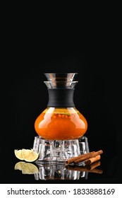 Tea With Sea Buckthorn On Dark Background. Orange Hot Water In Wineglass. Ingredient - Lime, Cinnamon - Are Reflected In Black Glass Table. Isolated Non Alcoholic Beverage.