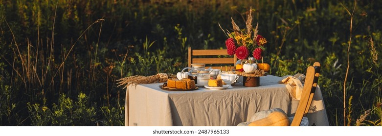 Tea setting with handmade pie. Beautiful view of garden wooden furniture with basket, soft blanket and burning candles. Outdoors fall family party, cozy autumn interior. Pumpkins, red dahlia banner