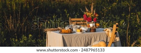 Tea setting with handmade pie. Beautiful view of garden wooden furniture with basket, soft blanket and burning candles. Outdoors fall family party, cozy autumn interior. Pumpkins, red dahlia banner