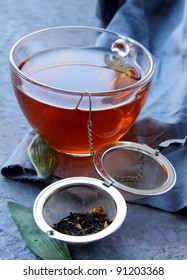 tea strainer with a fragrant black tea and cups in the background