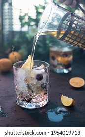 Tea From The Teapot Is Poured Into A Glass. The Process Of Making Iced Tea. In A Glass Of Ice, Berries And Lemon Slices.