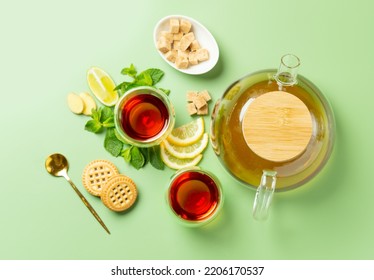 Tea time. Composition made with double wall glass of tea, transparent teapot, mint, lemon, ginger, cane sugar. Top view.