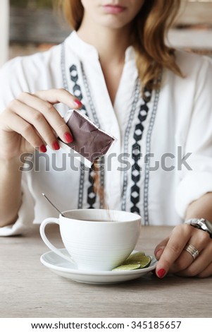 Tea time. Girl in cafe adding sugar in the cup of tea