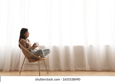 Tea time. Relaxed girl sitting in modern chair, enjoying hot coffee in front of window, side view, free space - Shutterstock ID 1655538490