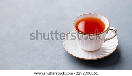 Tea in white cup with gold rim. Grey background. Copy space.