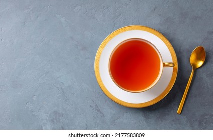 Tea in white cup with gold spoon. Grey background. Copy space. Top view.