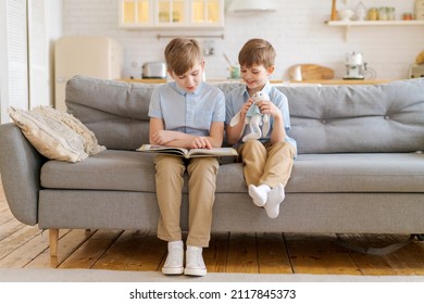 Teach your child to read book as teenager. Caucasian child looking into book while studying with teenager on couch in living room at home. Elder brother is reading book in living room on sofa brother - Shutterstock ID 2117845373