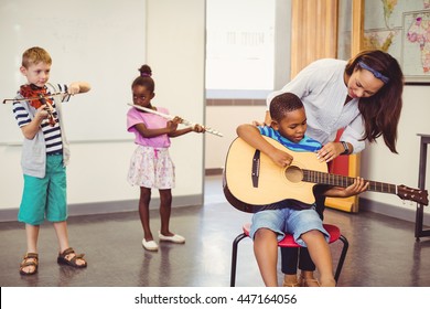 Teacher assisting a kids to play a musical instrument in classroom at school - Powered by Shutterstock