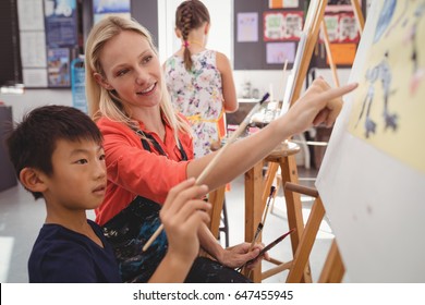 Teacher assisting schoolboy in drawing class at school - Powered by Shutterstock