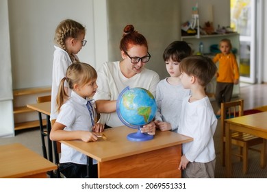 teacher and children in class are looking at globe, teacher helps explain the lesson to the children in the class at a desk. Educational school process, bright room and interesting learning