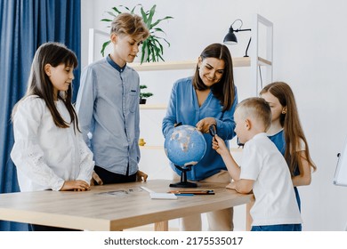 Teacher and children in class are looking at globe, teacher helps explain the lesson to the children in the class at a desk. Educational school process, bright room and interesting learning