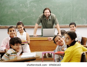 Teacher With Children In Classroom Using Laptop, Boys And Girls In School Together Learning