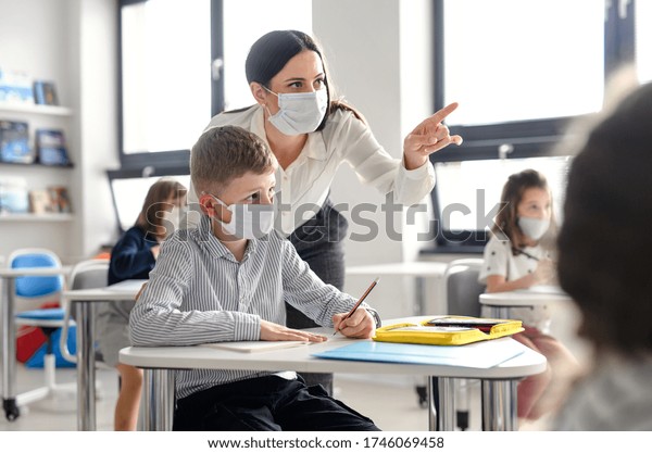 Teacher and children with face\
mask back at school after covid-19 quarantine and\
lockdown.