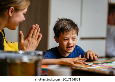 The teacher claps her hands and rejoices at the small victory of her student boy with down syndrome at painting studio for special need children. Development of children with spesial needs. - Powered by Shutterstock