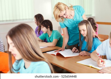 Teacher In Classroom Helping Student With The School Work.