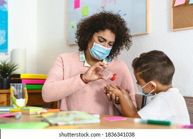 Teacher cleaning hands to student children with sanitizer gel while wearing face mask in preschool classroom during corona virus pandemic - Healthcare and education concept - Powered by Shutterstock