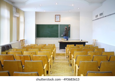 Teacher Clears With Blackboard In Empty Classroom, Back View