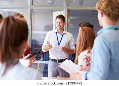 Teacher With College Students Standing By Desks In Classroom