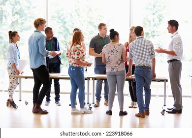 Teacher With College Students Standing By Desks In Classroom