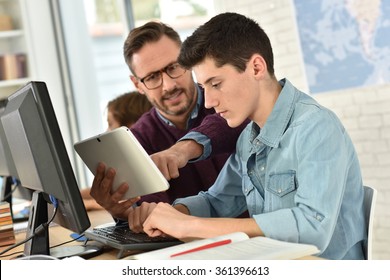 Teacher in computing class assisting teenager with tablet
