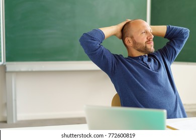 Teacher Or Creative Designer Taking A Break To Lean Back In His Chair With His Hands Behind His Head And A Chalkboard Background