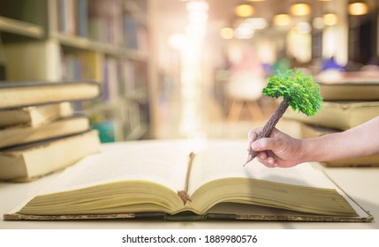 Teacher day concept: Student hand holding pencil of tree and writing on old book in blurred library background
