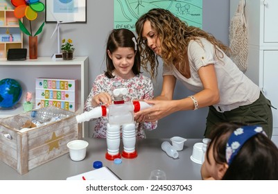 Teacher in ecology classroom helping to girl make recycled toy robot with plastic packages - Powered by Shutterstock