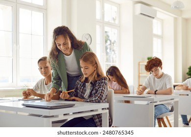 Teacher engages in teamwork in the school classroom, providing assistance to a schoolgirl during the lesson. This collaborative effort enhances the learning experience for pupils group.