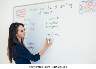 Teacher explaining differences between American and British spelling writing on whiteboard English language school
