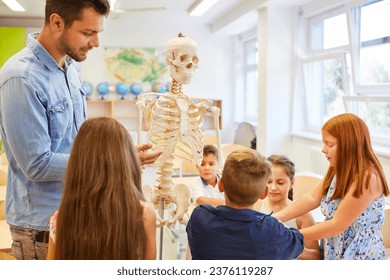 Teacher explaining human skeleton to kids in classroom at school - Powered by Shutterstock