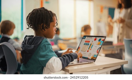 Teacher Explaining a Math Lesson to a Classroom Full of Bright Diverse Children in Primary School. Little Black Boy Browsing a Presentation on a Laptop Computer