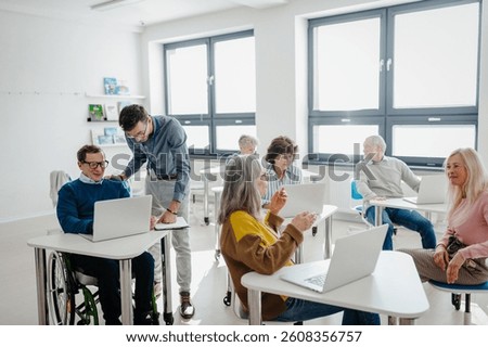 Teacher explaining senior students how to work with laptop and internet. Elderly people attending computer and technology education class. Digital literacy.