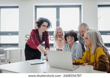 Teacher explaining senior students how to work with laptop, internetbanking. Elderly people attending computer and technology education class. Digital literacy.