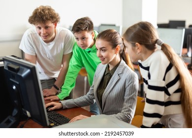 Teacher Explaining Task Solution To Young Girl And Boys During Computer Science Lesson In School.