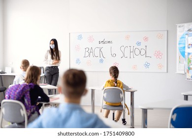 Teacher with face mask welcoming children back at school after lockdown. - Shutterstock ID 1751409800
