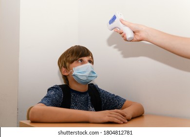 Teacher with facemask scanning a kid with digital thermometer, measuring body temperature before lessons. New normal, back to school during coronavirus pandemic. - Powered by Shutterstock