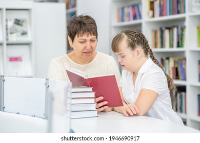 Teacher And Girl With Syndrome Down Read A Book At Library. Education For Disabled Children Concept