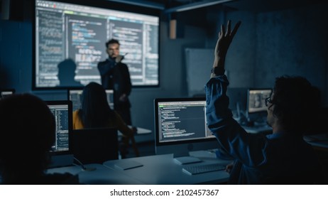 Teacher Giving Computer Science Lecture to Diverse Multiethnic Group of Female and Male Classmates in Dark College Room. Student Raises Hand and Answers Lecturer a Question About Software Engineering. - Shutterstock ID 2102457367