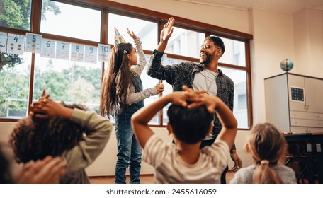 Teacher giving a high five to a student on her birthday. Celebration in an elementary school class. Young girl wearing a cone hat, she is enjoying her birthday with her teacher and classmates. - Powered by Shutterstock