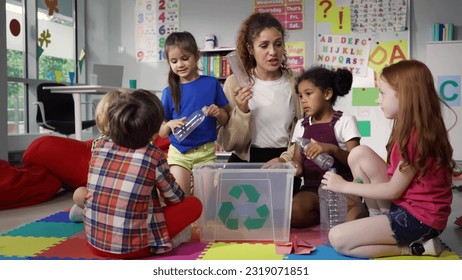 Teacher giving recycle lesson to little kids in kindergarten. Protect nature, save environment. Diverse preschool children learn to sort garbage in primary school putting plastic bottles in recycle - Powered by Shutterstock