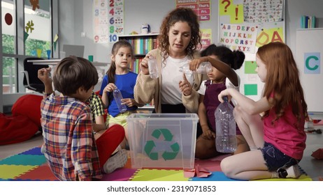 Teacher giving recycle lesson to little kids in kindergarten. Protect nature, save environment. Diverse preschool children learn to sort garbage in primary school putting plastic bottles in recycle - Powered by Shutterstock