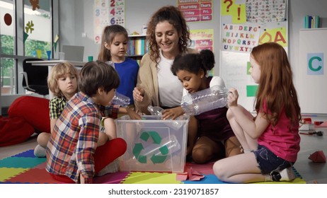Teacher giving recycle lesson to little kids in kindergarten. Protect nature, save environment. Diverse preschool children learn to sort garbage in primary school putting plastic bottles in recycle - Powered by Shutterstock