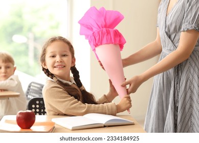 Teacher greeting her happy pupil with pink school cone in classroom - Powered by Shutterstock