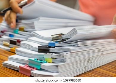 Teacher Hand Holds Pen For Checking Student's Homework Assignment On Table Office. Paper Documents Stacked In Archive With Paperclip. Report Papers Stacks. Business And Education Concept.