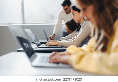 Teacher helping children with coding exercises at their desks. In this computer literacy class, he provides attention to the students, fostering a positive learning environment for the young minds.