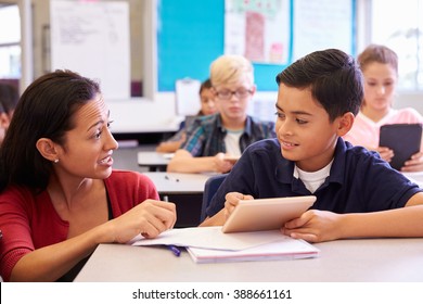 Teacher helping elementary school boy using tablet computer